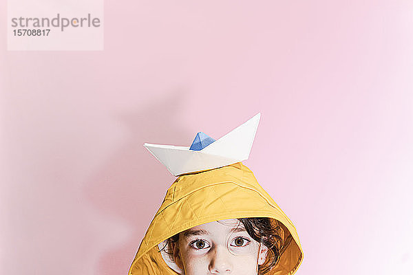 Kleines Mädchen  das ein Ölzeug trägt und ein Papierboot auf dem Kopf trägt
