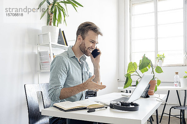 Lächelnder Mann am Telefon am Schreibtisch im Büro