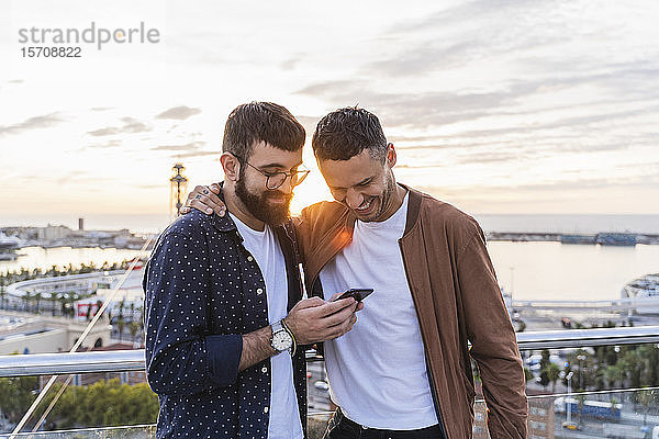 Schwules Ehepaar mit Handy auf dem Aussichtspunkt über der Stadt mit Blick auf den Hafen  Barcelona  Spanien
