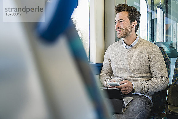Lächelnder junger Mann mit Smartphone und Tablet im Zug