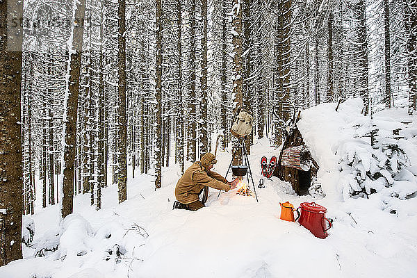 Mann bereitet im Winterwald neben einem Holzunterstand Tee zu  Bundesland Salzburg  Österreich