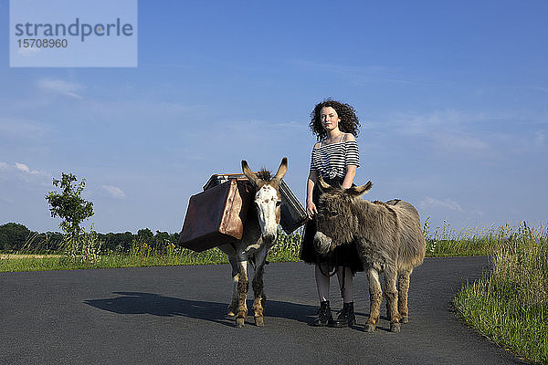Junge Frau steht auf Landstraße mit Eseln  die Gepäck tragen