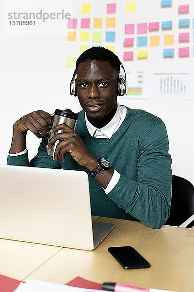 Porträt eines Mannes mit Kaffeetasse und Laptop am Schreibtisch im Büro sitzend