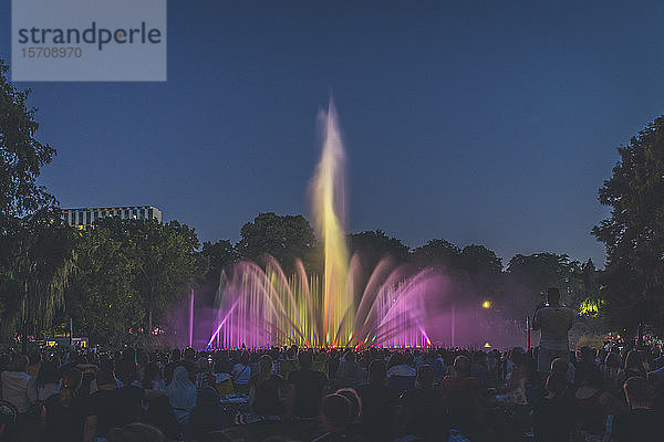 Deutschland  Hamburg  Menschen beobachten beleuchteten Springbrunnen bei Nacht
