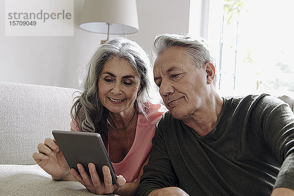 Glückliches älteres Ehepaar entspannt zu Hause auf der Couch mit Tablette