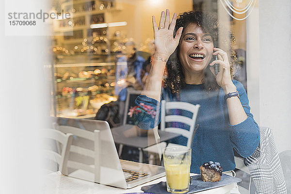 Glückliche Frau am Telefon in einem Café winkt
