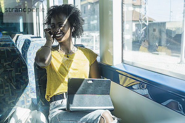 Glückliche junge Frau mit Kopfhörern und Tablette im Zug