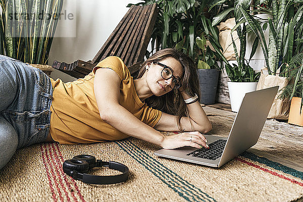 Entspannte junge Frau liegt zu Hause mit Laptop auf dem Boden