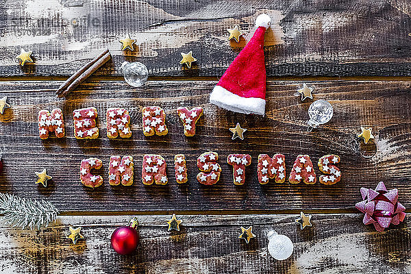Fröhliche Weihnachten geschrieben mit Keksen und Weihnachtsdekoration auf Holzoberfläche