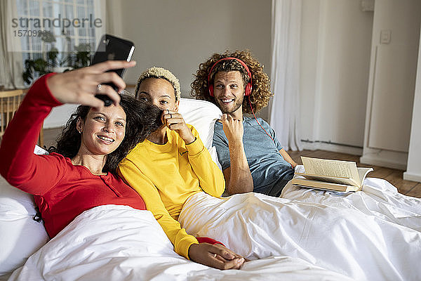 Glückliche Freunde entspannen zu Hause im Bett mit Smartphone
