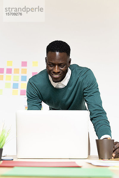Lächelnder Mann arbeitet am Laptop am Schreibtisch im Büro