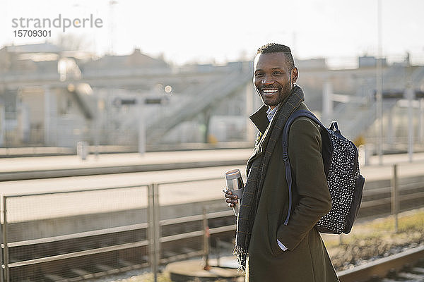 Porträt eines lächelnden Mannes mit wiederverwendbarem Becher  der auf den Zug wartet