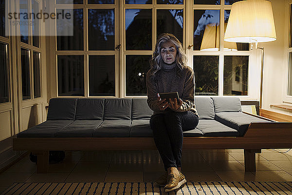 Reife Frau benutzt Tablette auf der Couch zu Hause im Dunkeln