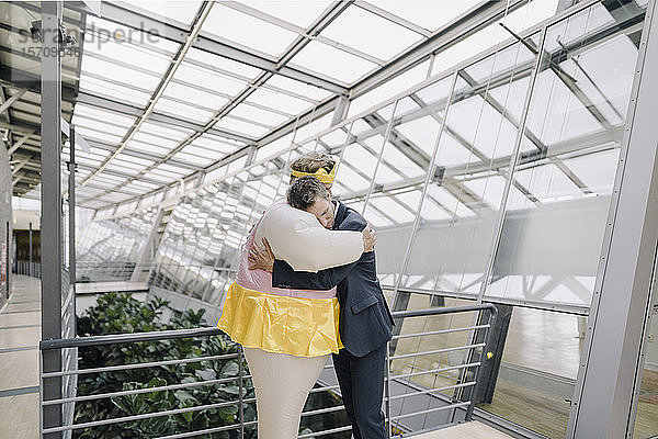 Als Ballerina verkleideter Geschäftsmann und Mann umarmen sich in modernem Bürogebäude