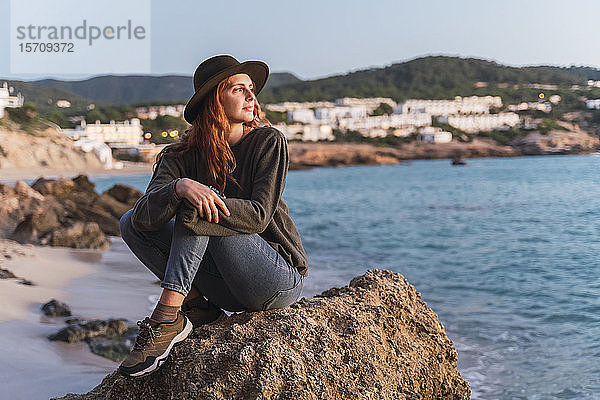 Junge Frau sitzt am Strand und genießt den Sonnenuntergang  Ibiza
