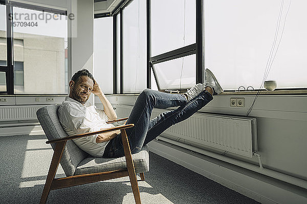 Reifer Geschäftsmann entspannt sich am Fenster in leerem Büro
