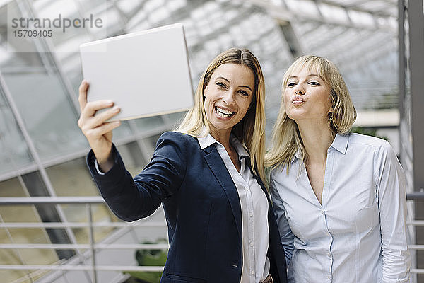 Zwei glückliche junge Geschäftsfrauen benutzen ein Tablett im Büro