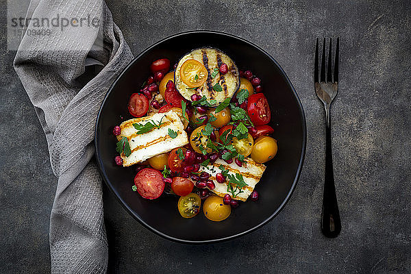 Schale mit persischem Salat mit Tomaten  gegrilltem Halloumi-Käse  Auberginen  Granatapfelkernen  Sumach  schwarzem Sesam und Petersilie