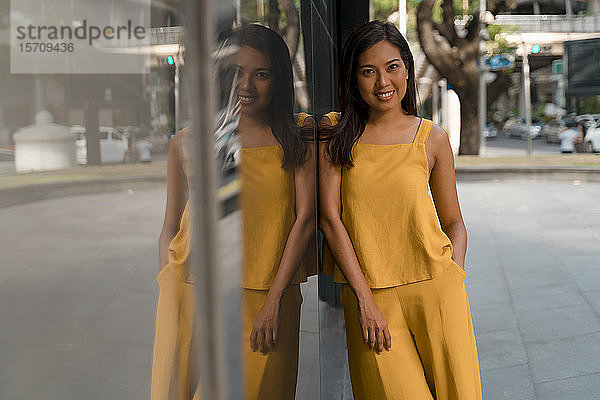 Porträt einer modischen  gelb gekleideten Frau  die an einer Glasfront lehnt