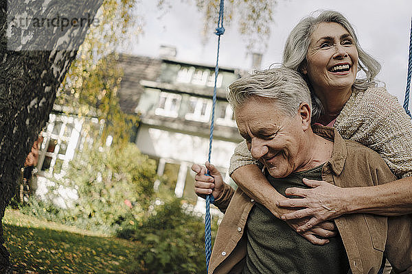 Glückliche Frau umarmt älteren Mann auf einer Schaukel im Garten