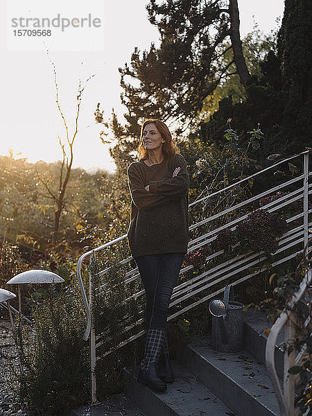 Glückliche Frau steht auf der Treppe in ihrem Garten und lächelt