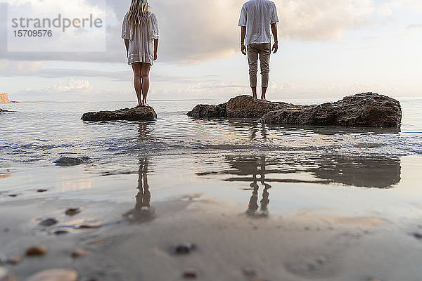 Rückenansicht eines jungen Paares  das auf Felsen vor dem Meer steht  Ibiza  Balearen  Spanien