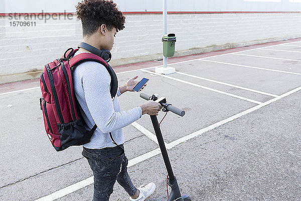 Junger Mann mit E-Scooter mit Smartphone