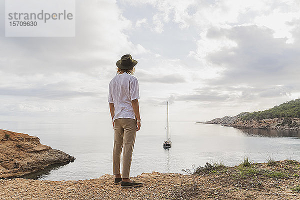 Rückansicht eines jungen Mannes  der vor dem Meer steht und auf das Meer blickt  Ibiza  Balearen  Spanien