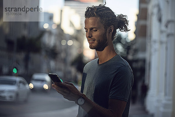 Selbstbewusster junger Mann nutzt Smartphone in der Stadt