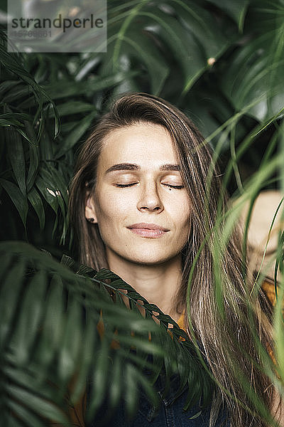 Porträt einer jungen Frau mit geschlossenen Augen inmitten grüner Pflanzen
