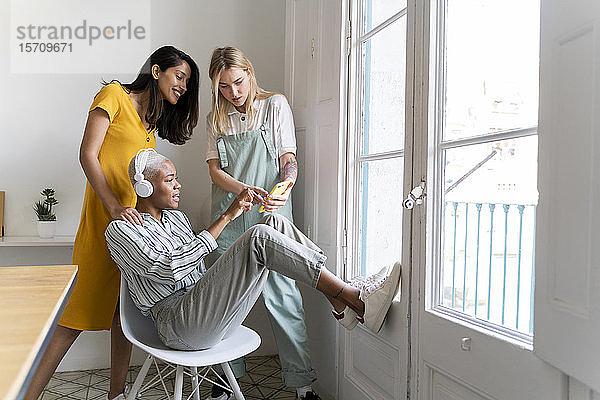 Drei Frauen mit Kopfhörern und Handy am Fenster