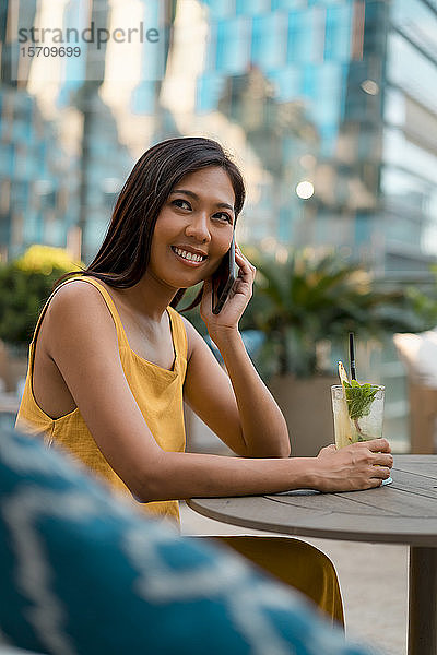 Porträt einer lächelnden Frau am Telefon  die mit einem Getränk in einem Cafe sitzt