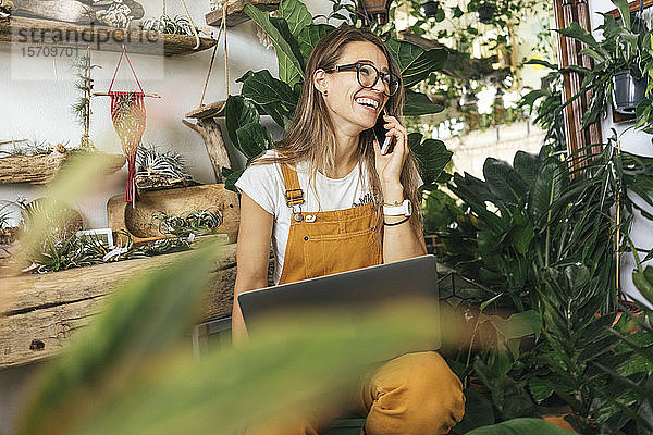 Lachende junge Frau am Telefon in einem kleinen Gartenbaubetrieb