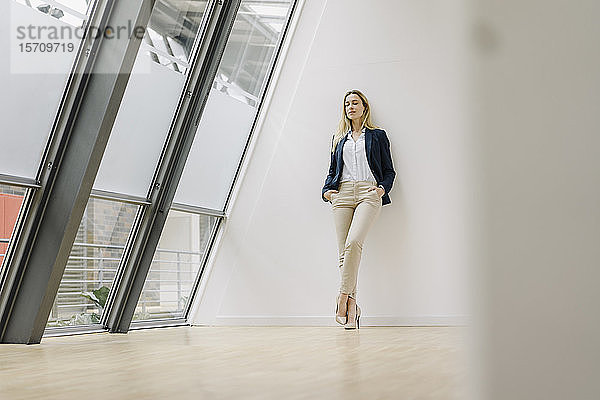 Junge Geschäftsfrau lehnt an einer Wand in einem modernen Bürogebäude