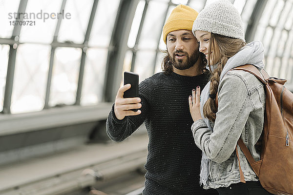 Glückliches junges Paar mit Smartphone am Bahnsteig  Berlin  Deutschland