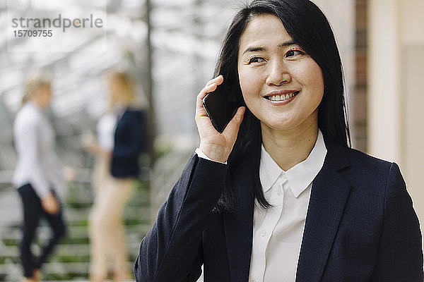 Porträt einer lächelnden Geschäftsfrau am Telefon im Büro mit Kollegen im Hintergrund