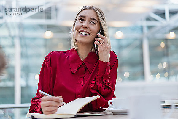 Lächelnde junge Geschäftsfrau mit Notebook am Telefon