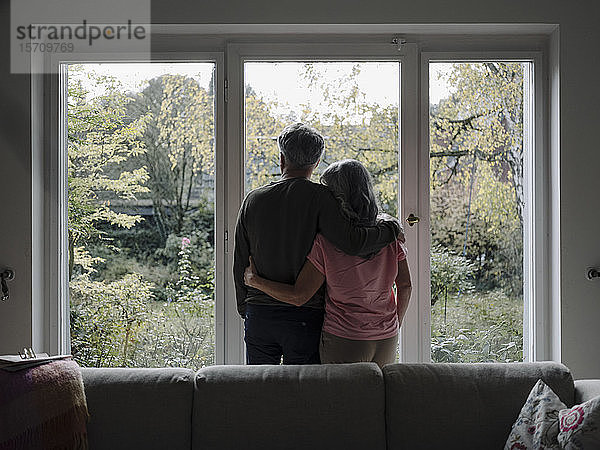 Rückansicht eines älteren Ehepaares  das zu Hause aus dem Fenster schaut