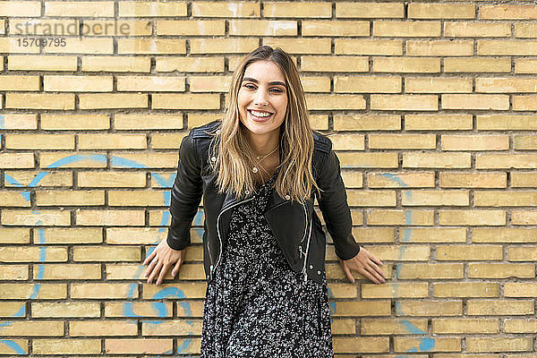 Porträt einer lachenden jungen Frau vor einer Ziegelmauer
