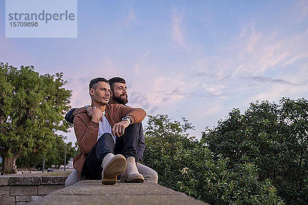 Anhängliches schwules Paar sitzt bei Sonnenuntergang an einer Wand
