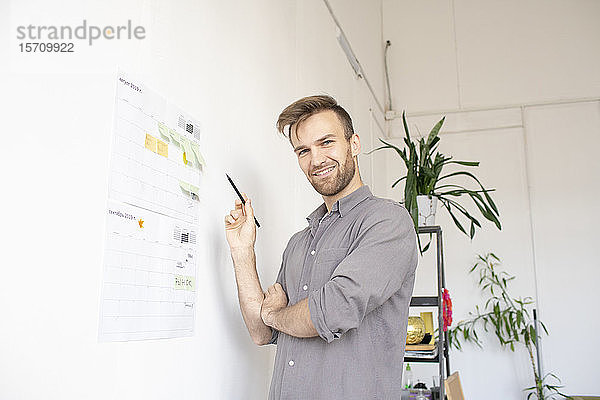 Porträt eines lächelnden Mannes bei der Arbeit auf Papier an der Wand im Büro