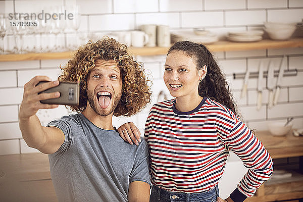 Verspieltes Paar  das zu Hause in der Küche ein Selfie macht