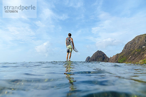 Surfer mit seinem Surfbrett in der Hand  auf Stein stehend  Insel Sumbawa  Indonesien  über-unteres Bild