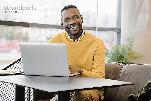 Porträt eines glücklichen Mannes mit Laptop in einem Cafe