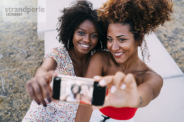 Junge Frauen  die lächeln und sich mit ihrem Smartphone in einem Park ein Selfie machen  Fokus auf den Hintergrund