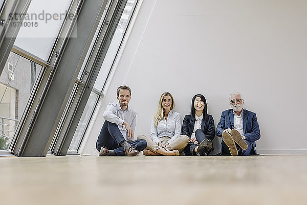 Porträt von lächelnden Geschäftsleuten  die im Büro auf dem Boden sitzen