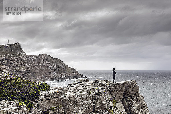 Mann steht auf felsiger Klippe und schaut zum Horizont  Cape Point  Westkap  Südafrika