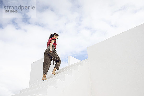 Barfüßiger Geschäftsmann steigt weiße Treppe unter bewölktem Himmel