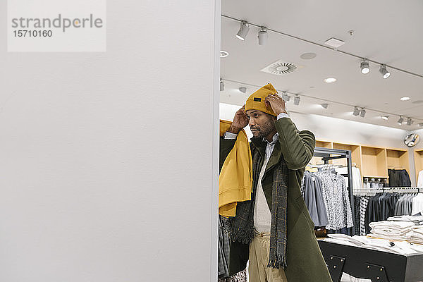 Stilvoller Mann beim Einkaufen in einem Bekleidungsgeschäft  der eine Mütze anprobiert