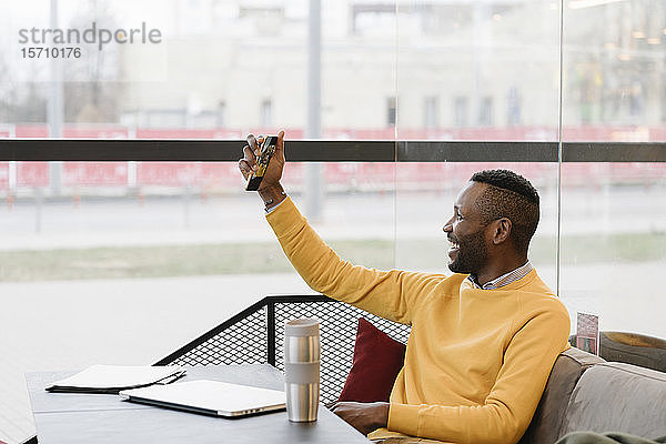 Glücklicher Mann benutzt Smartphone in einem Cafe